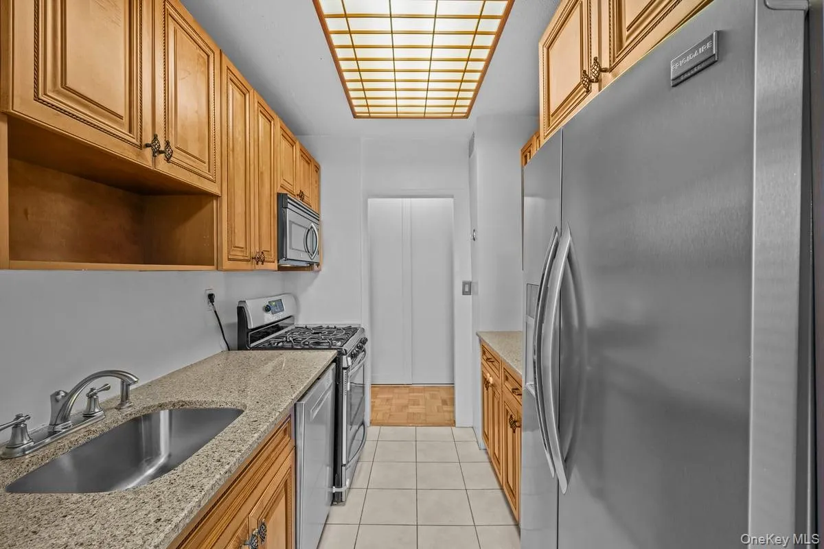 Kitchen with appliances with stainless steel finishes, light stone countertops, brown cabinets, and open shelves Kitchen with appliances with stainless steel finishes, light stone countertops, brown cabinets, and open shelves