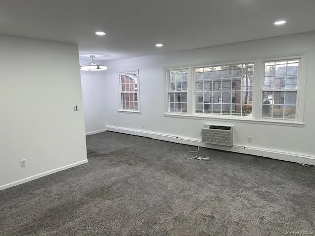 Unfurnished room featuring recessed lighting, dark colored carpet, a wall mounted AC, and baseboard heating Unfurnished room featuring recessed lighting, dark colored carpet, a wall mounted AC, and baseboard heating