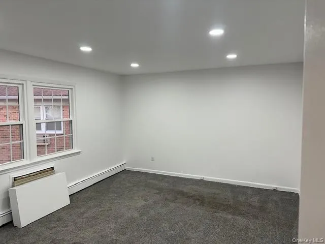Empty room featuring dark carpet, recessed lighting, and baseboard heating Empty room featuring dark carpet, recessed lighting, and baseboard heating
