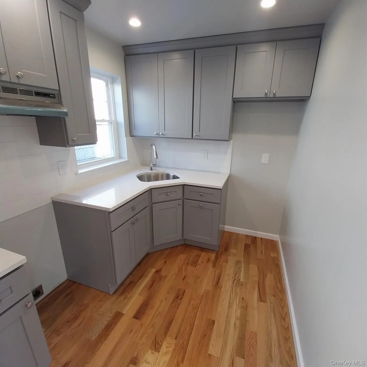 Kitchen with gray cabinets, light wood-type flooring, under cabinet range hood, recessed lighting, and light stone counters Kitchen with gray cabinets, light wood-type flooring, under cabinet range hood, recessed lighting, and light stone counters