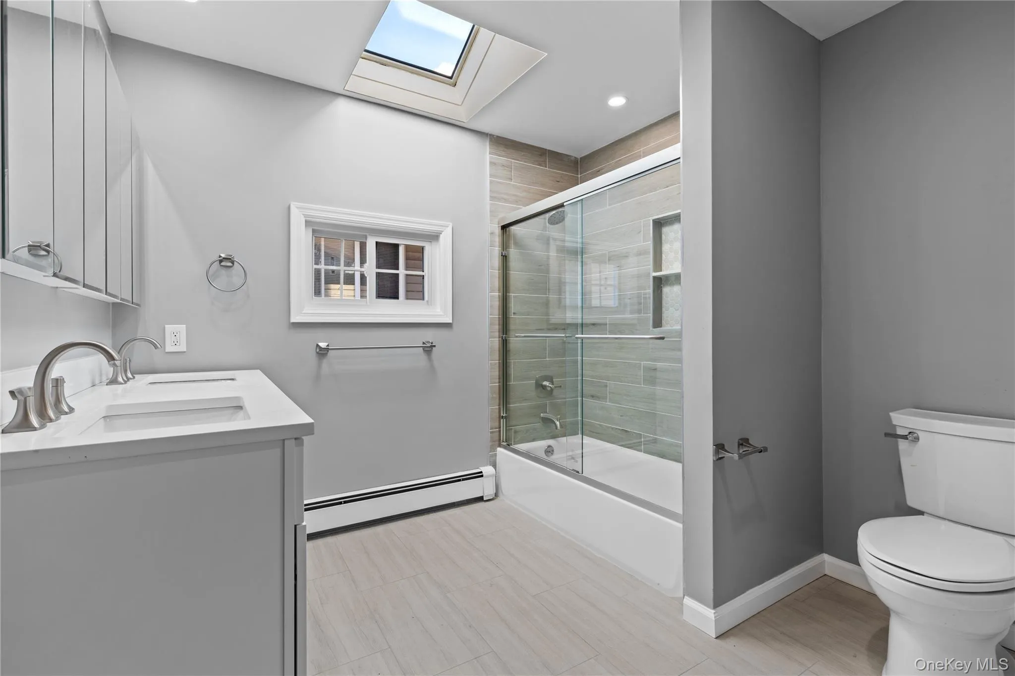 Full bath featuring double vanity, baseboard heating, combined bath / shower with glass door, a skylight, and recessed lighting Full bath featuring double vanity, baseboard heating, combined bath / shower with glass door, a skylight, and recessed lighting