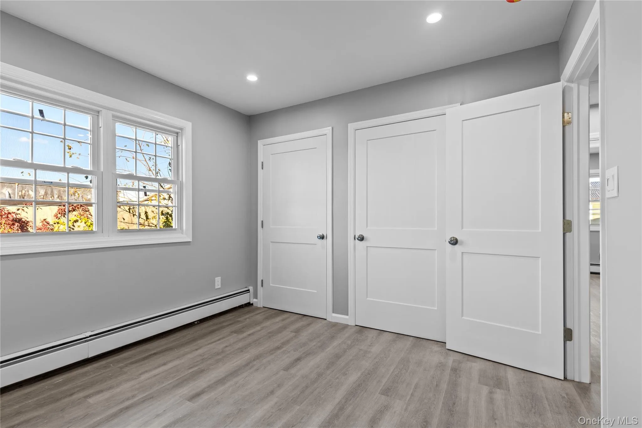 Unfurnished bedroom with baseboard heating, light wood-style floors, recessed lighting, and two closets Unfurnished bedroom with baseboard heating, light wood-style floors, recessed lighting, and two closets