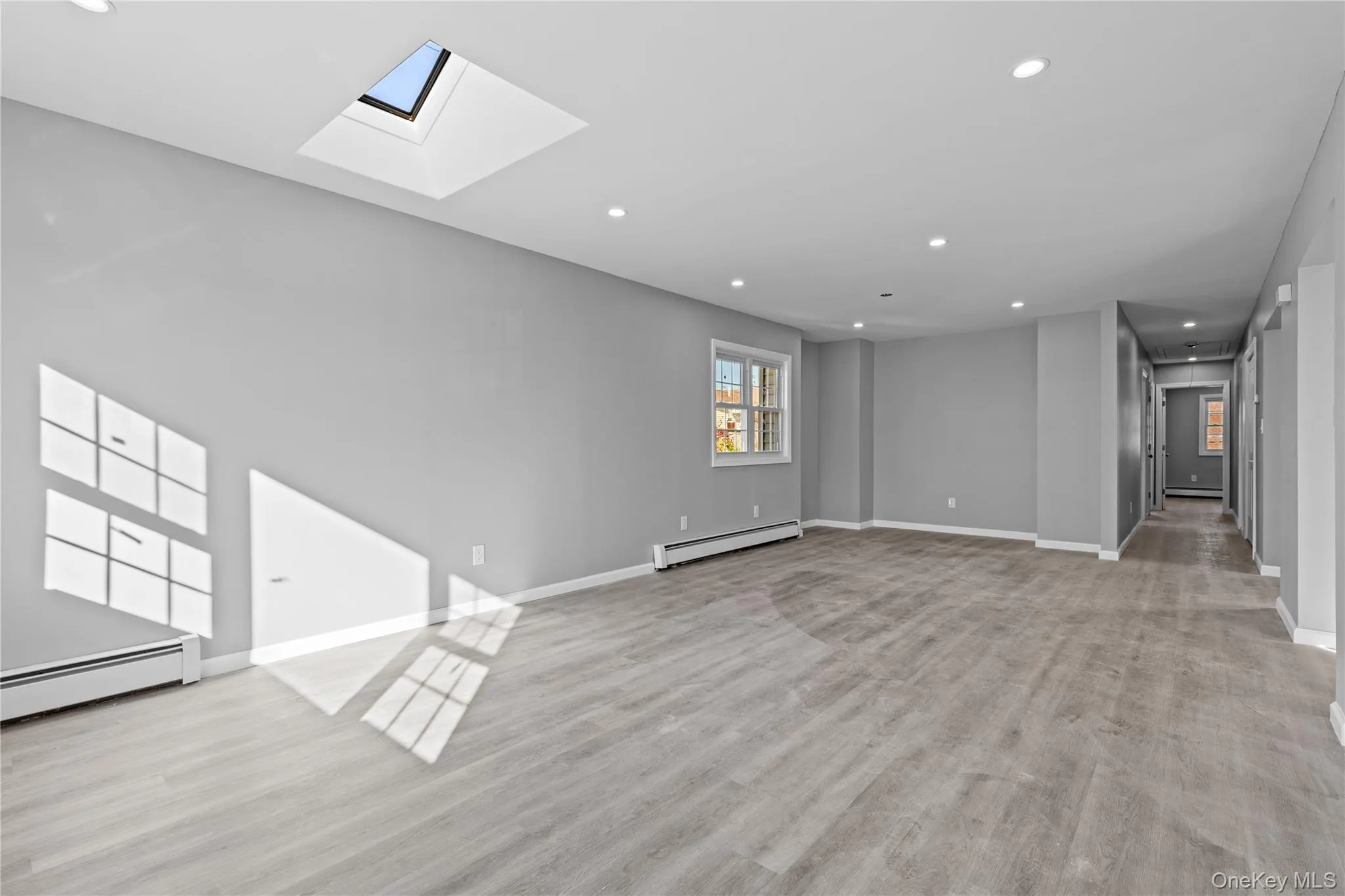 Unfurnished living room with recessed lighting, a skylight, light wood-style floors, and a baseboard heating unit Unfurnished living room with recessed lighting, a skylight, light wood-style floors, and a baseboard heating unit