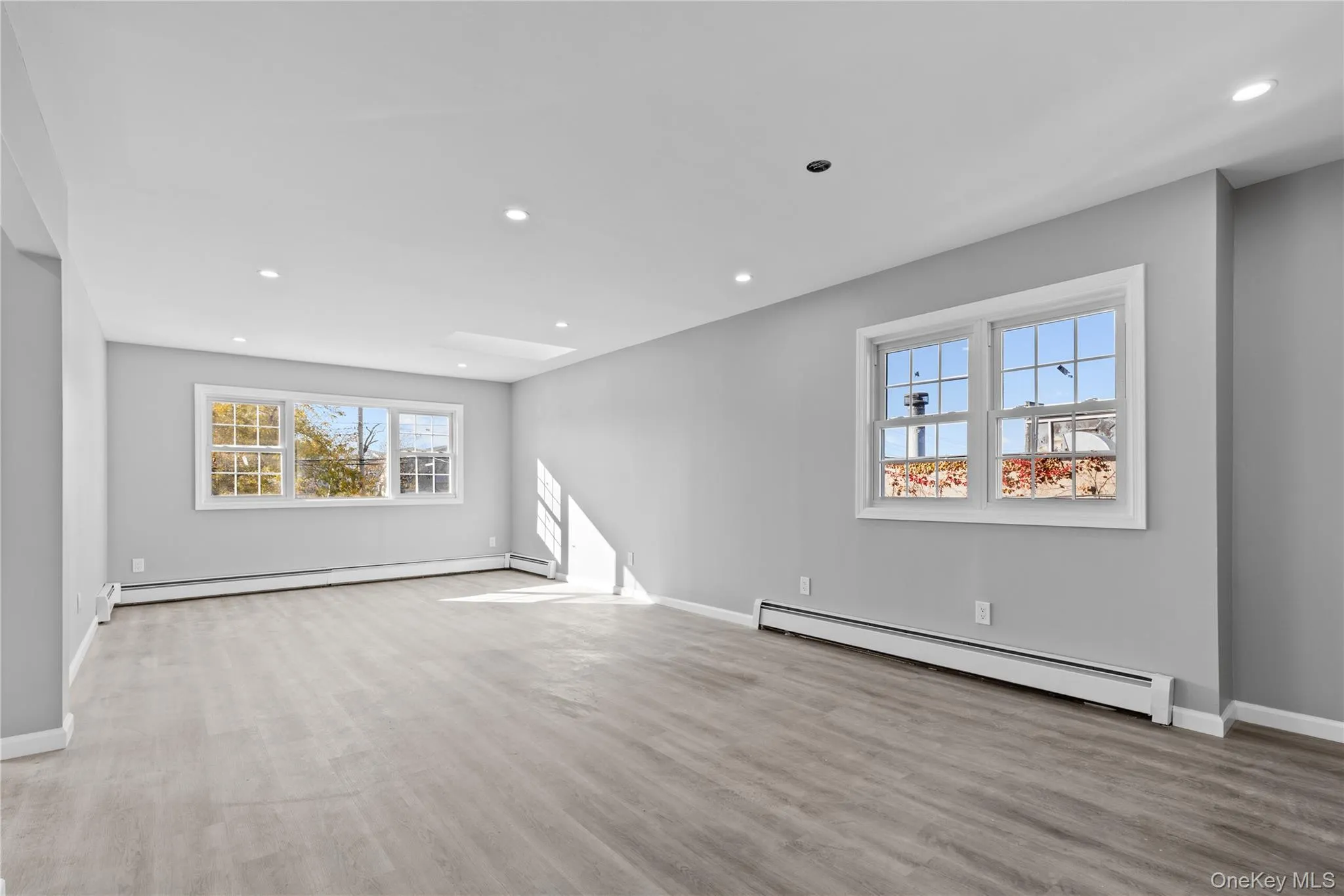 Unfurnished living room with baseboard heating, healthy amount of natural light, recessed lighting, and light wood-style flooring Unfurnished living room with baseboard heating, healthy amount of natural light, recessed lighting, and light wood-style flooring