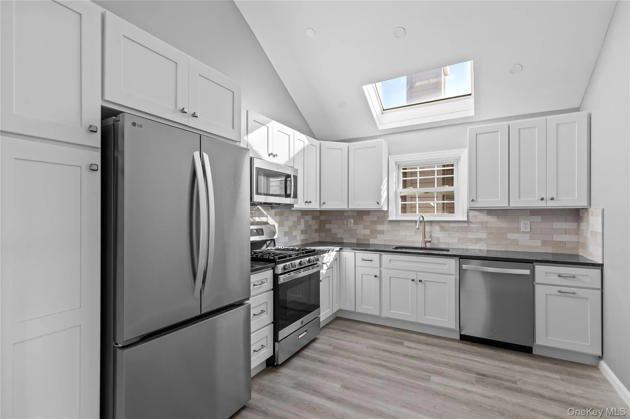 Kitchen featuring appliances with stainless steel finishes, white cabinetry, backsplash, a skylight, and light wood-type flooring Kitchen featuring appliances with stainless steel finishes, white cabinetry, backsplash, a skylight, and light wood-type flooring