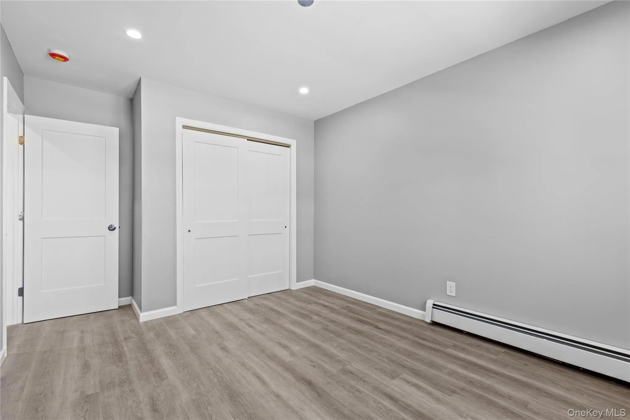Unfurnished bedroom with recessed lighting, light wood-style flooring, a baseboard radiator, and a closet Unfurnished bedroom with recessed lighting, light wood-style flooring, a baseboard radiator, and a closet