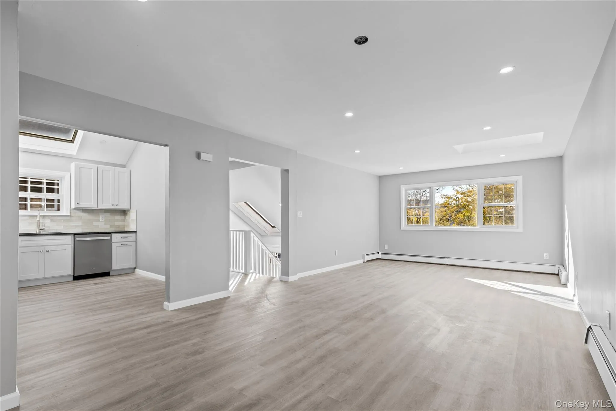 Unfurnished living room featuring a skylight, baseboard heating, light wood-style floors, and recessed lighting Unfurnished living room featuring a skylight, baseboard heating, light wood-style floors, and recessed lighting