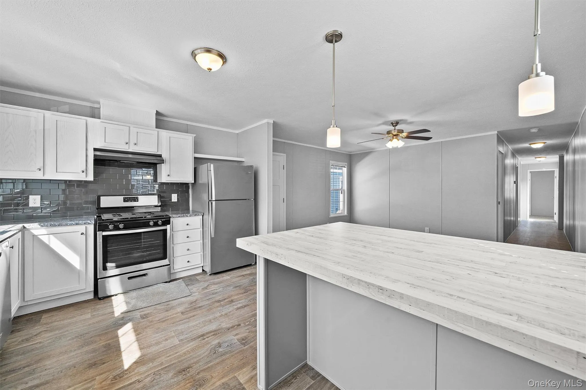Kitchen featuring hanging light fixtures, a ceiling fan, light wood-style floors, under cabinet range hood, and stainless steel appliances Kitchen featuring hanging light fixtures, a ceiling fan, light wood-style floors, under cabinet range hood, and stainless steel appliances