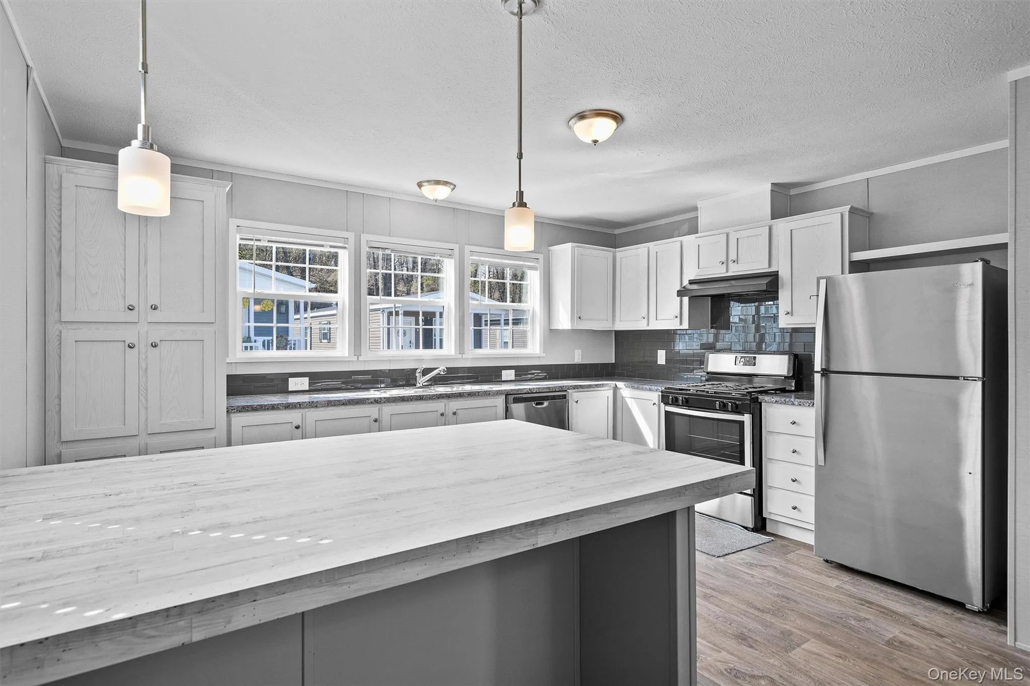 Kitchen with pendant lighting, light wood finished floors, under cabinet range hood, and stainless steel appliances Kitchen with pendant lighting, light wood finished floors, under cabinet range hood, and stainless steel appliances