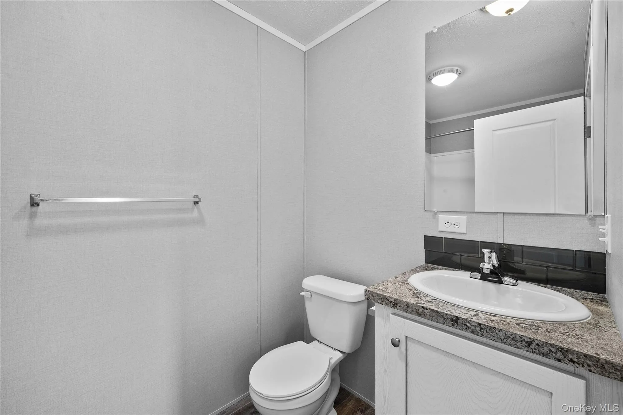 Bathroom with vanity, ornamental molding, toilet, decorative backsplash, and wood finished floors Bathroom with vanity, ornamental molding, toilet, decorative backsplash, and wood finished floors