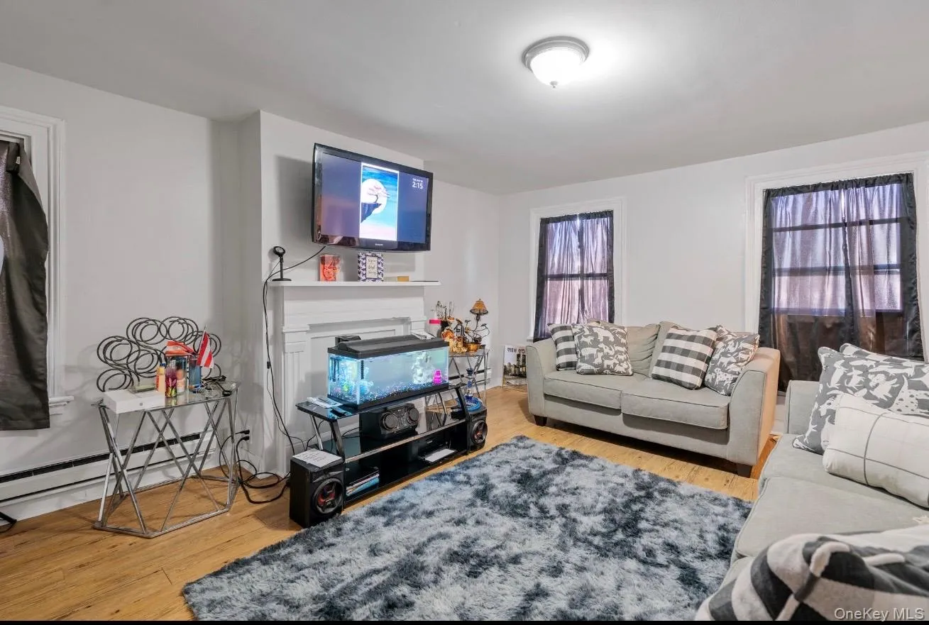 Living room with light wood-style floors, a baseboard heating unit, and a fireplace Living room with light wood-style floors, a baseboard heating unit, and a fireplace
