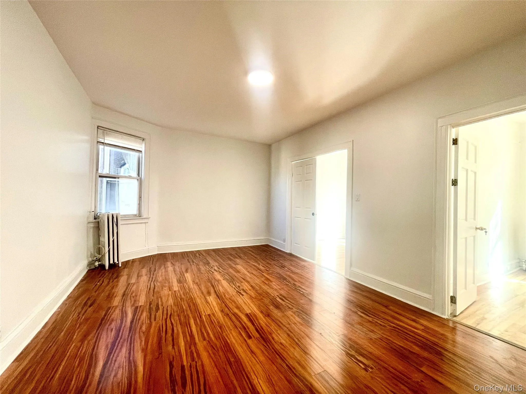 Unfurnished bedroom featuring wood finished floors and radiator Unfurnished bedroom featuring wood finished floors and radiator