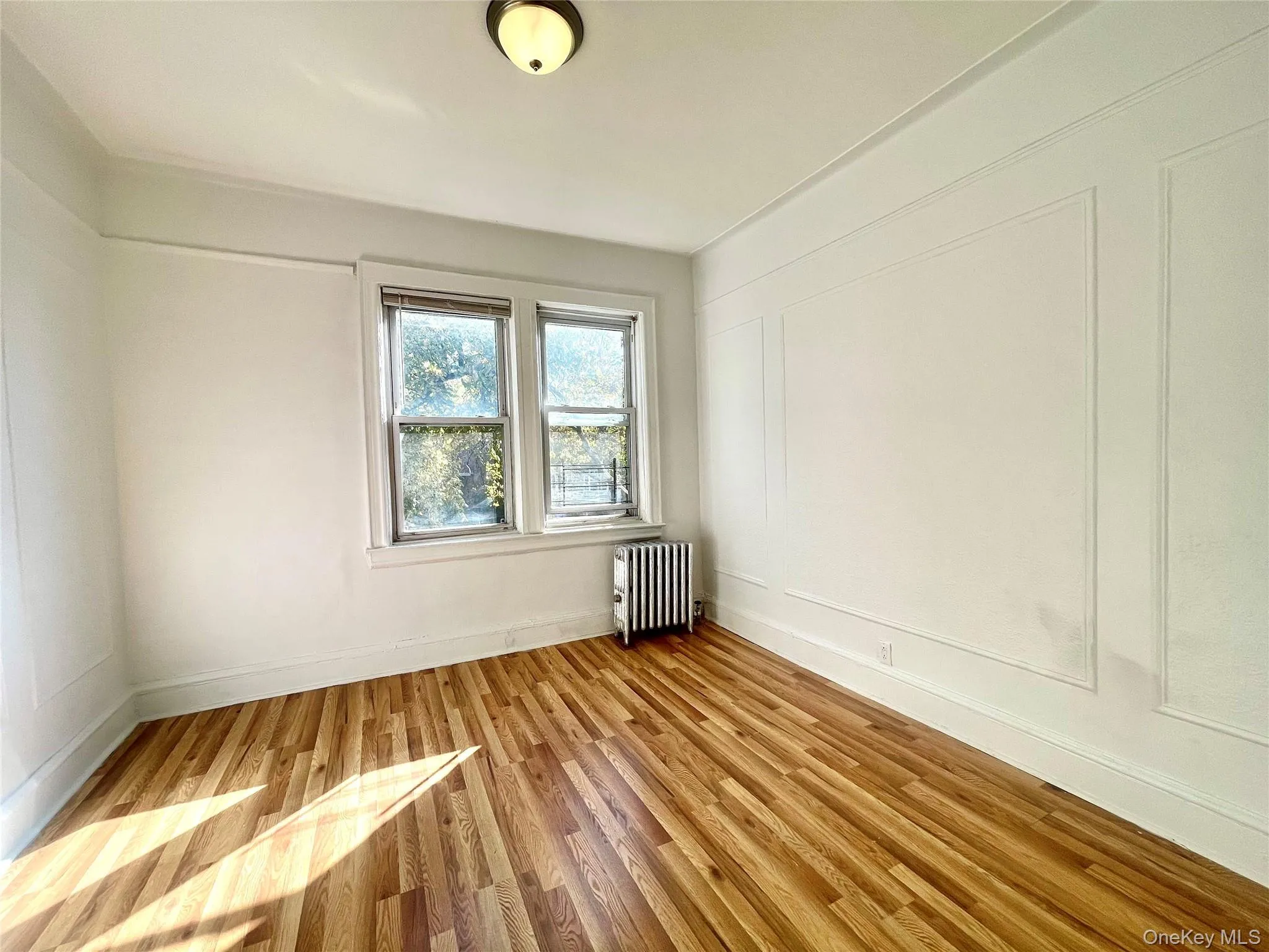 Empty room featuring a decorative wall, light wood-style floors, and radiator heating unit Empty room featuring a decorative wall, light wood-style floors, and radiator heating unit
