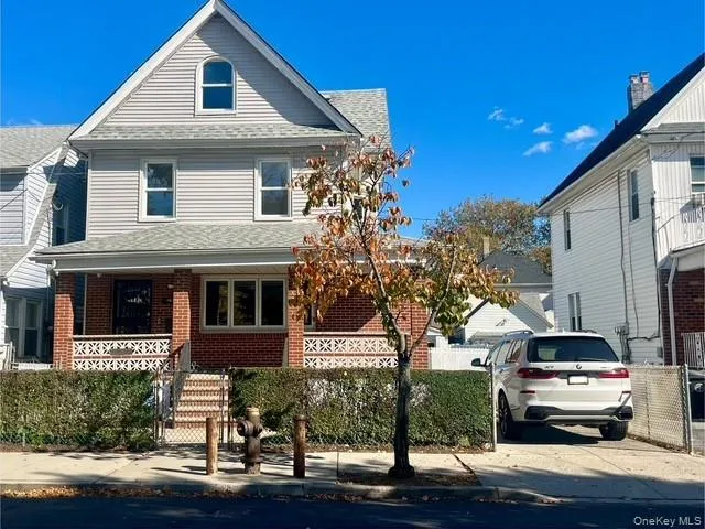 View of front of home featuring covered porch, a shingled roof, brick siding, and stairway