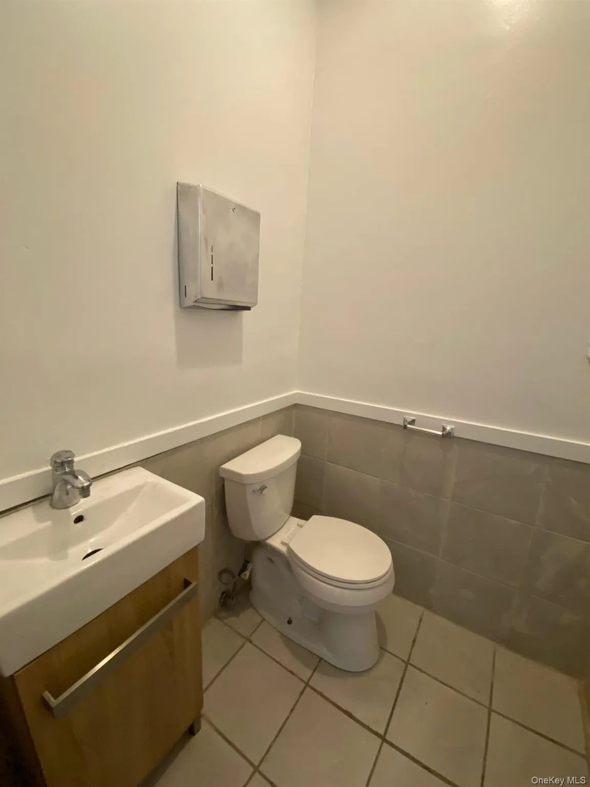 Half bathroom featuring light tile patterned floors, vanity, wainscoting, and tile walls Half bathroom featuring light tile patterned floors, vanity, wainscoting, and tile walls