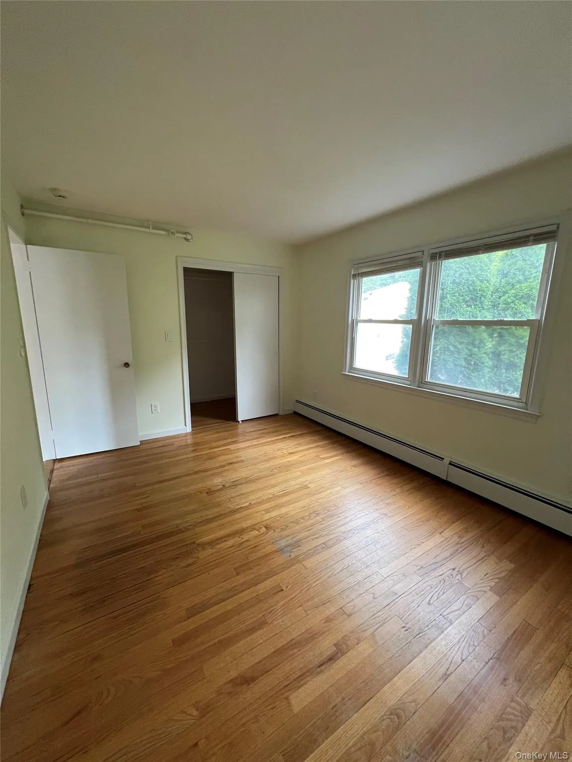 Unfurnished bedroom with a baseboard heating unit, light wood-style flooring, and a closet Unfurnished bedroom with a baseboard heating unit, light wood-style flooring, and a closet