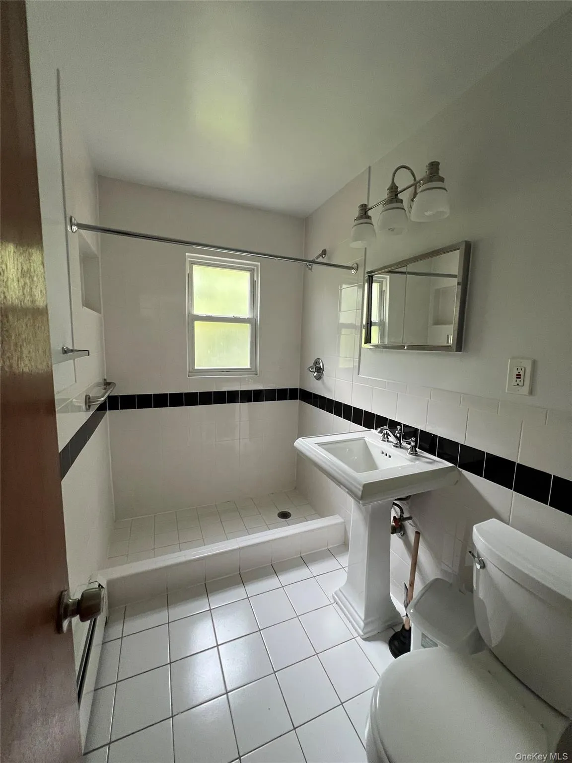 Full bath with tile walls, a stall shower, light tile patterned floors, wainscoting, and baseboard heating Full bath with tile walls, a stall shower, light tile patterned floors, wainscoting, and baseboard heating
