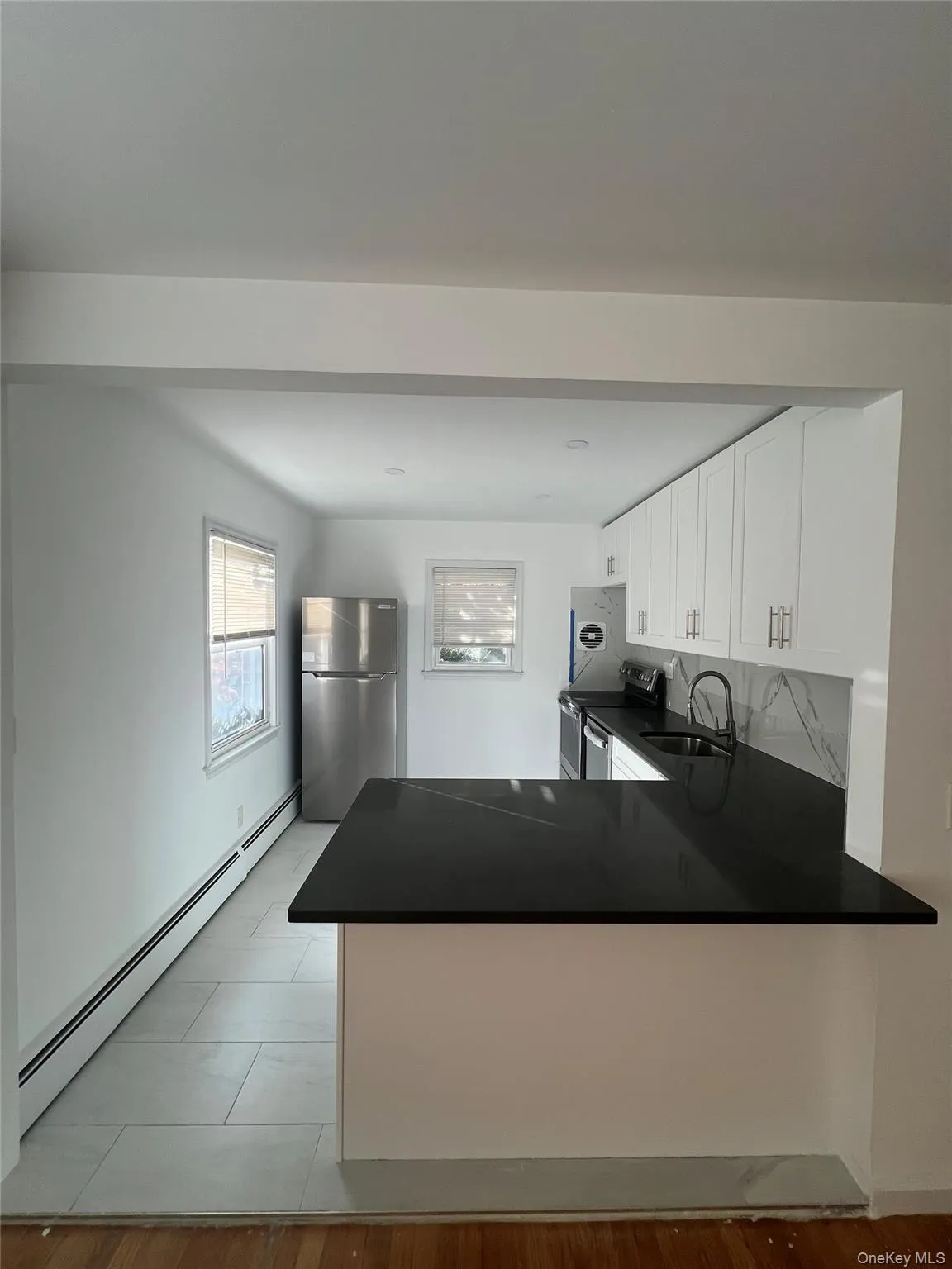 Kitchen featuring a baseboard heating unit, stainless steel appliances, dark countertops, and a peninsula Kitchen featuring a baseboard heating unit, stainless steel appliances, dark countertops, and a peninsula
