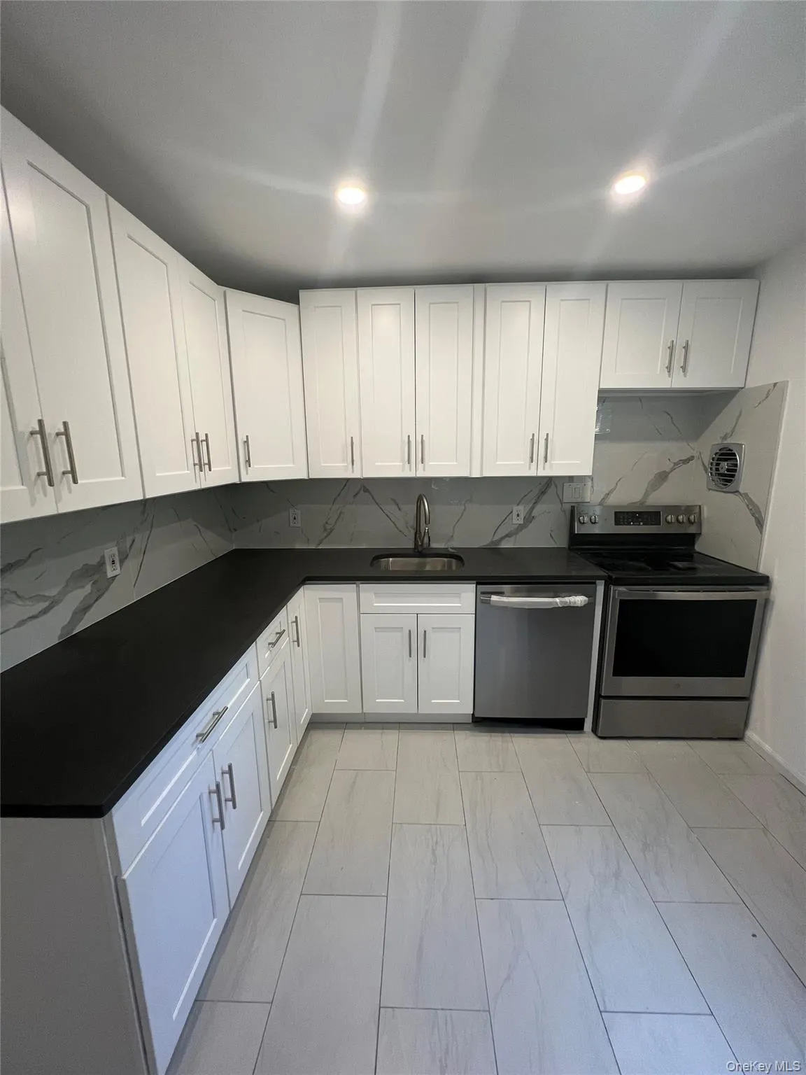 Kitchen with decorative backsplash, stainless steel appliances, white cabinetry, light marble finish floors, and dark stone counters Kitchen with decorative backsplash, stainless steel appliances, white cabinetry, light marble finish floors, and dark stone counters