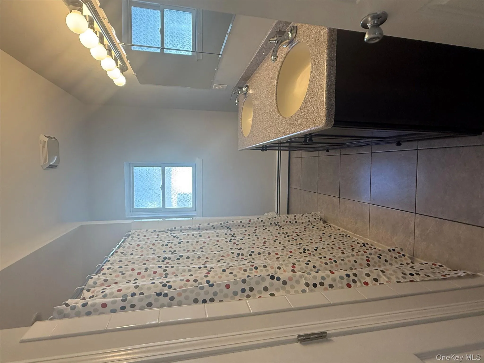 Bathroom featuring dark tile patterned floors, double vanity, a shower with curtain, a baseboard radiator, and lofted ceiling Bathroom featuring dark tile patterned floors, double vanity, a shower with curtain, a baseboard radiator, and lofted ceiling