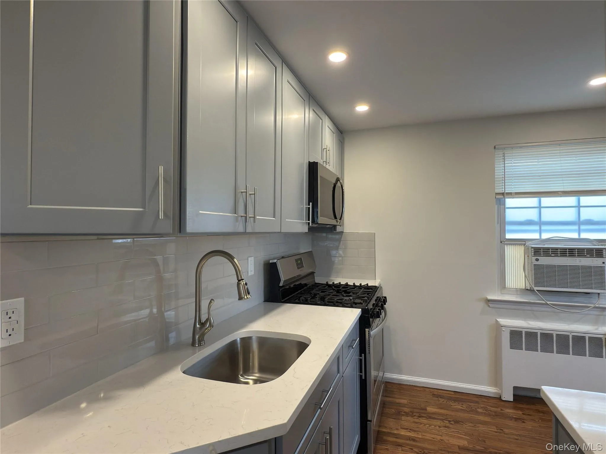 Kitchen featuring stainless steel gas range oven, gray cabinets, radiator, decorative backsplash, and dark wood-type flooring Kitchen featuring stainless steel gas range oven, gray cabinets, radiator, decorative backsplash, and dark wood-type flooring