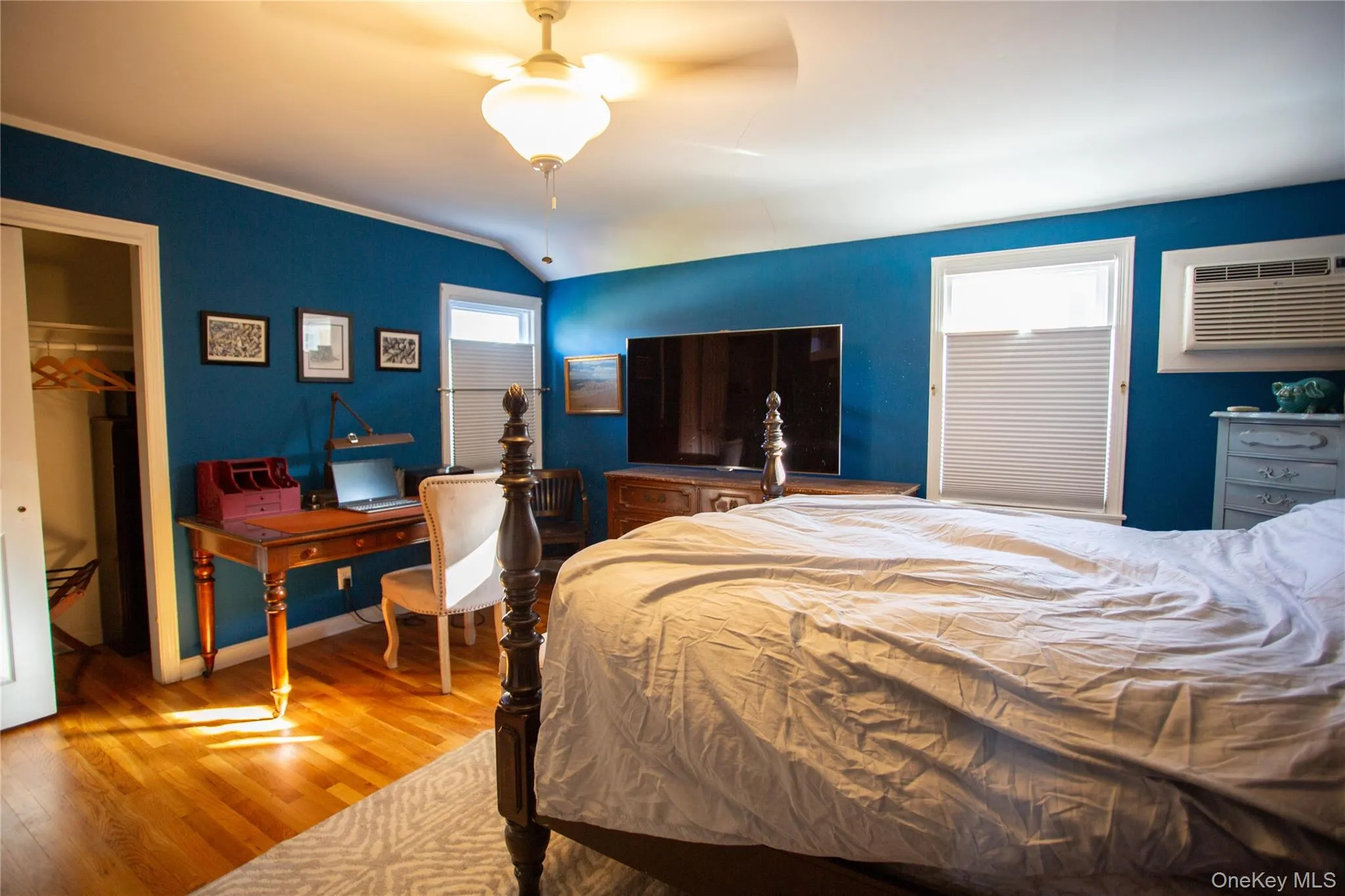 Bedroom featuring light wood-style flooring, a closet, lofted ceiling, a ceiling fan, and an AC wall unit Bedroom featuring light wood-style flooring, a closet, lofted ceiling, a ceiling fan, and an AC wall unit