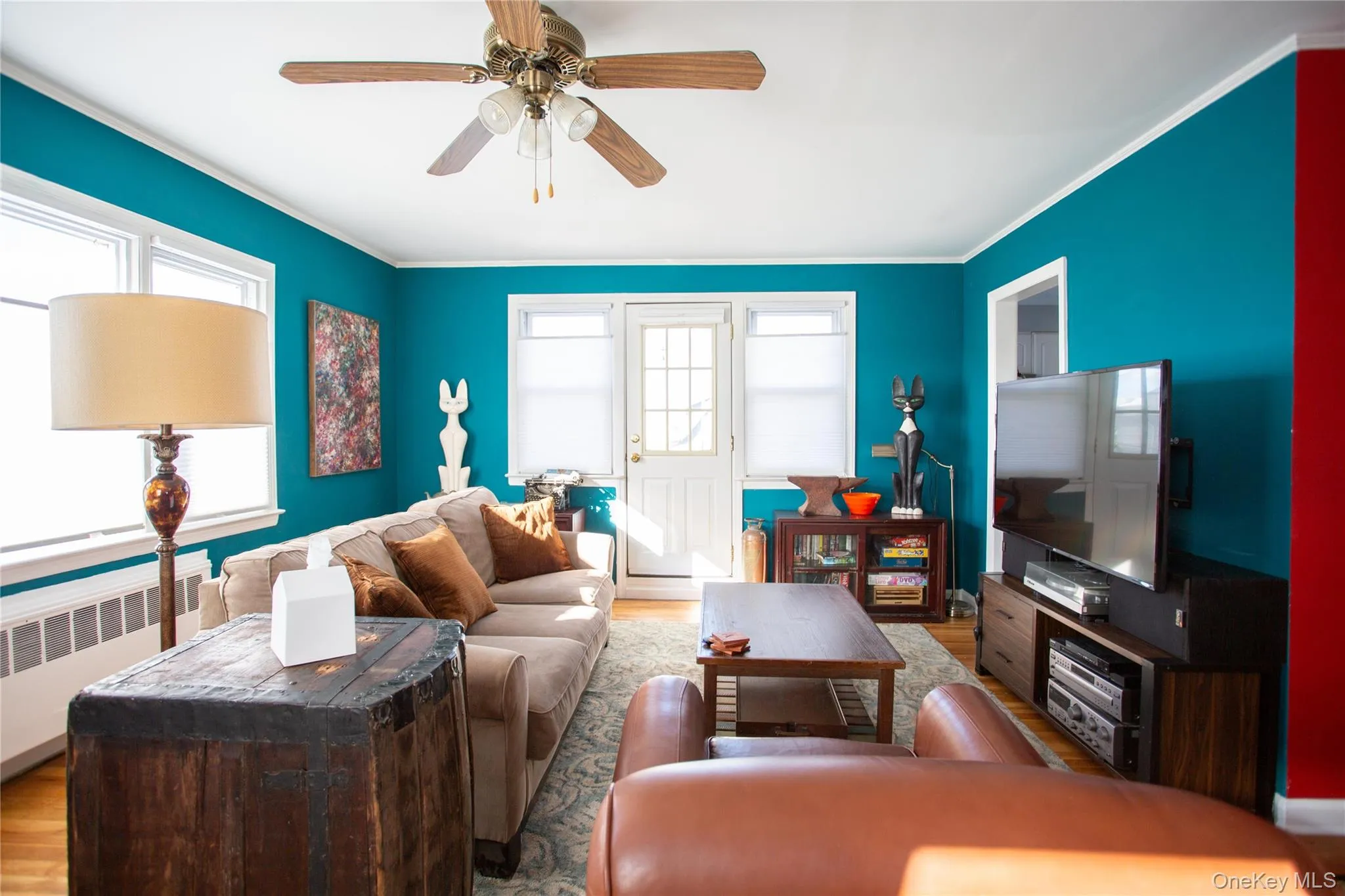 Living area featuring ornamental molding, radiator heating unit, a ceiling fan, and wood finished floors Living area featuring ornamental molding, radiator heating unit, a ceiling fan, and wood finished floors