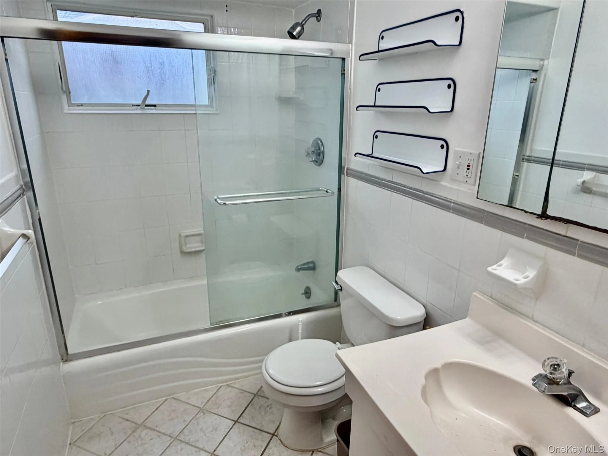 Full bathroom featuring vanity, light tile patterned floors, tile walls, and shower / bath combination with glass door Full bathroom featuring vanity, light tile patterned floors, tile walls, and shower / bath combination with glass door