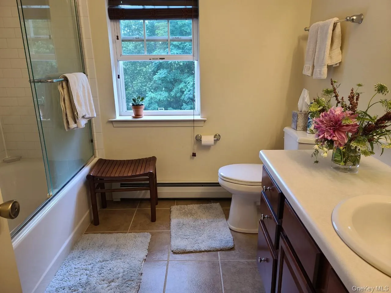 Full bathroom with enclosed tub / shower combo, vanity, dark tile patterned flooring, and a baseboard heating unit Full bathroom with enclosed tub / shower combo, vanity, dark tile patterned flooring, and a baseboard heating unit