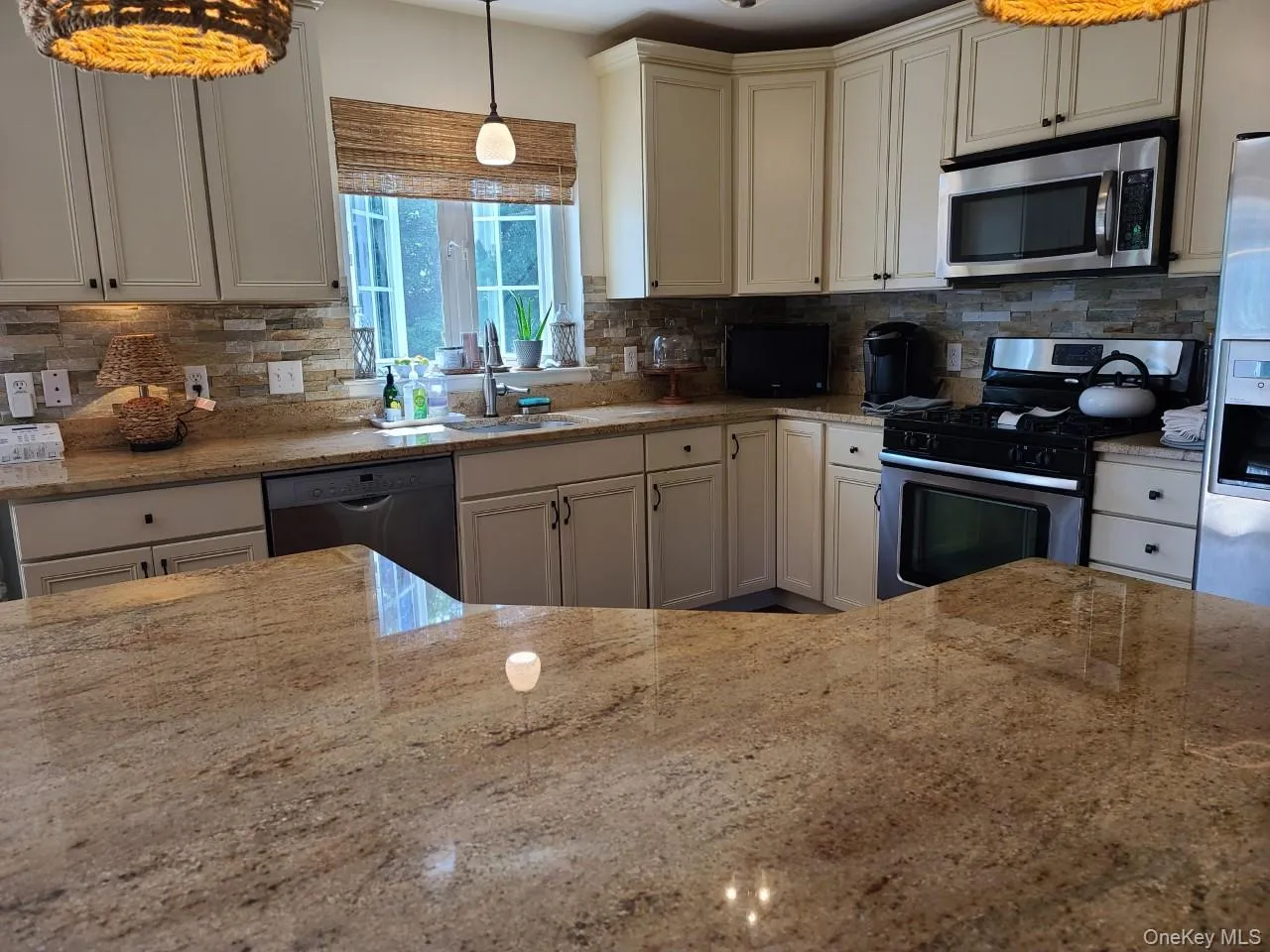 Kitchen with stainless steel appliances, light stone countertops, hanging light fixtures, and tasteful backsplash Kitchen with stainless steel appliances, light stone countertops, hanging light fixtures, and tasteful backsplash