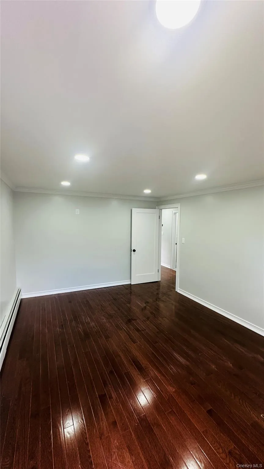 Basement with dark wood-style floors, a baseboard radiator, recessed lighting, and ornamental molding Basement with dark wood-style floors, a baseboard radiator, recessed lighting, and ornamental molding
