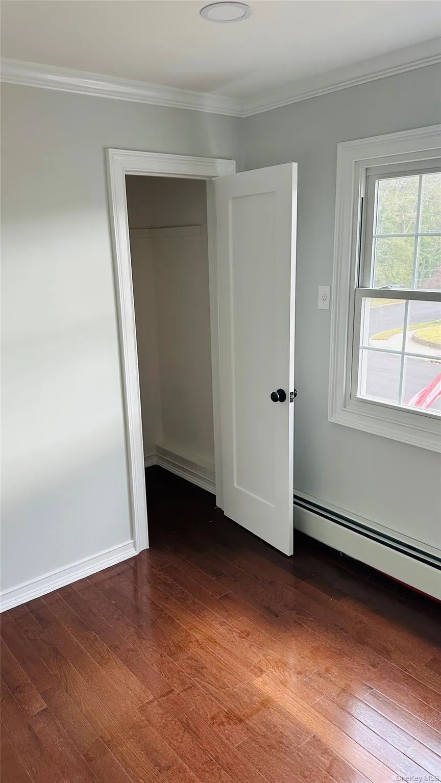 Unfurnished bedroom featuring crown molding, baseboard heating, and dark wood-style flooring Unfurnished bedroom featuring crown molding, baseboard heating, and dark wood-style flooring