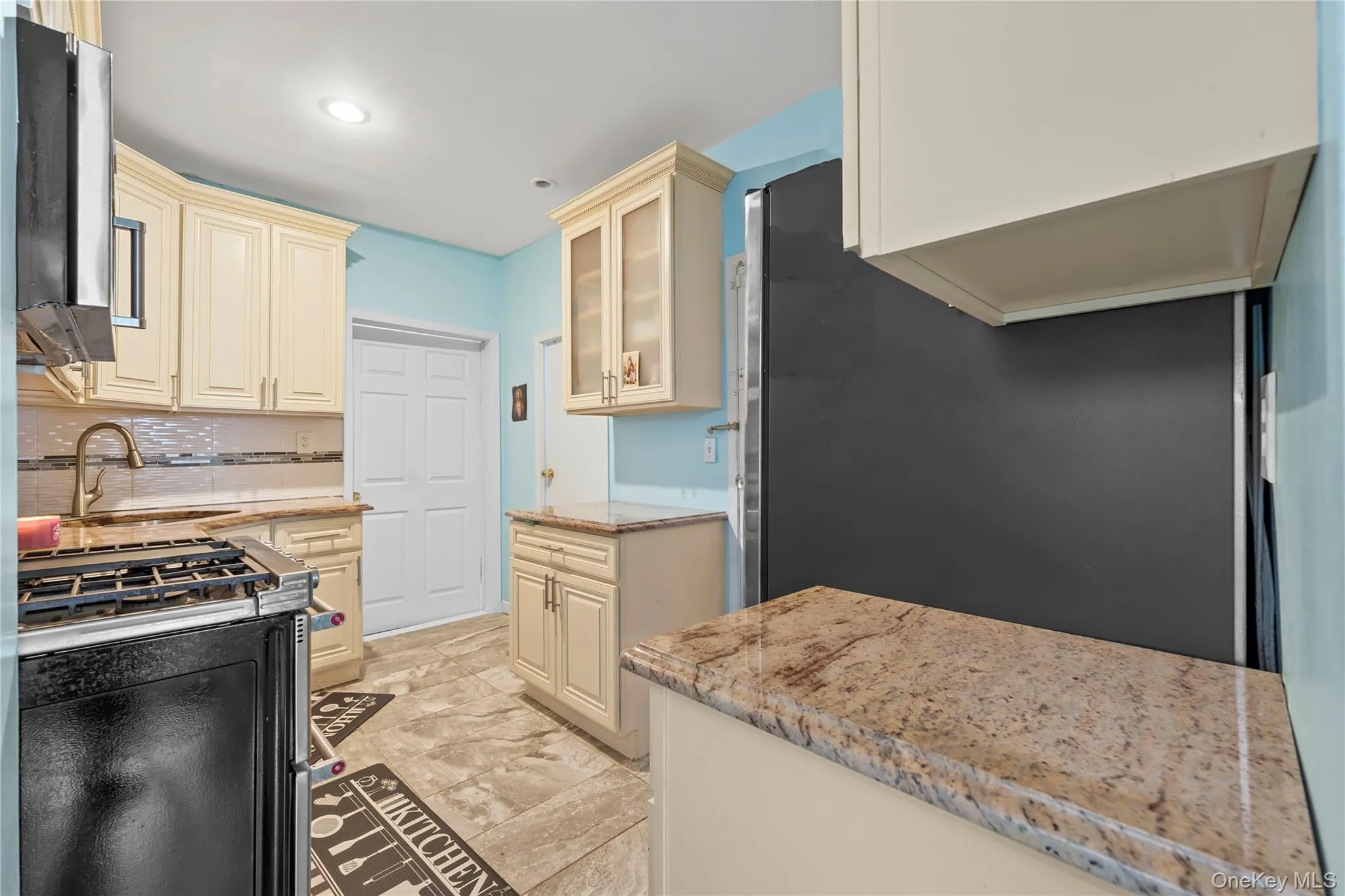 Kitchen with appliances with stainless steel finishes, cream cabinetry, glass insert cabinets, decorative backsplash, and recessed lighting Kitchen with appliances with stainless steel finishes, cream cabinetry, glass insert cabinets, decorative backsplash, and recessed lighting