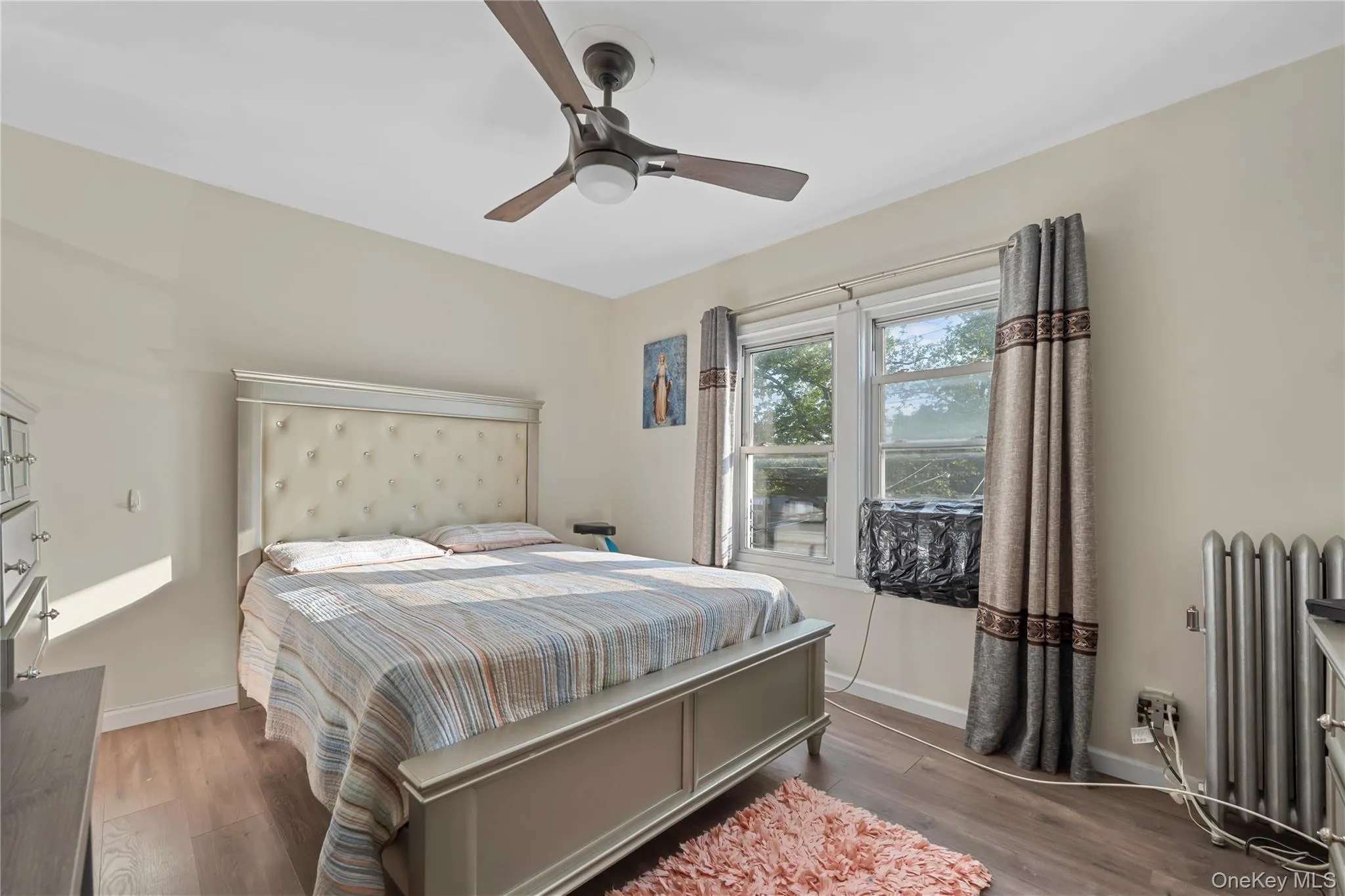 Bedroom featuring radiator heating unit, wood finished floors, and ceiling fan Bedroom featuring radiator heating unit, wood finished floors, and ceiling fan
