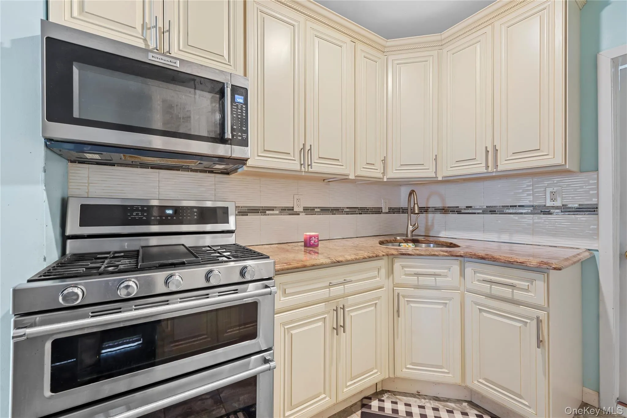 Kitchen with cream cabinets, appliances with stainless steel finishes, decorative backsplash, and light stone counters Kitchen with cream cabinets, appliances with stainless steel finishes, decorative backsplash, and light stone counters