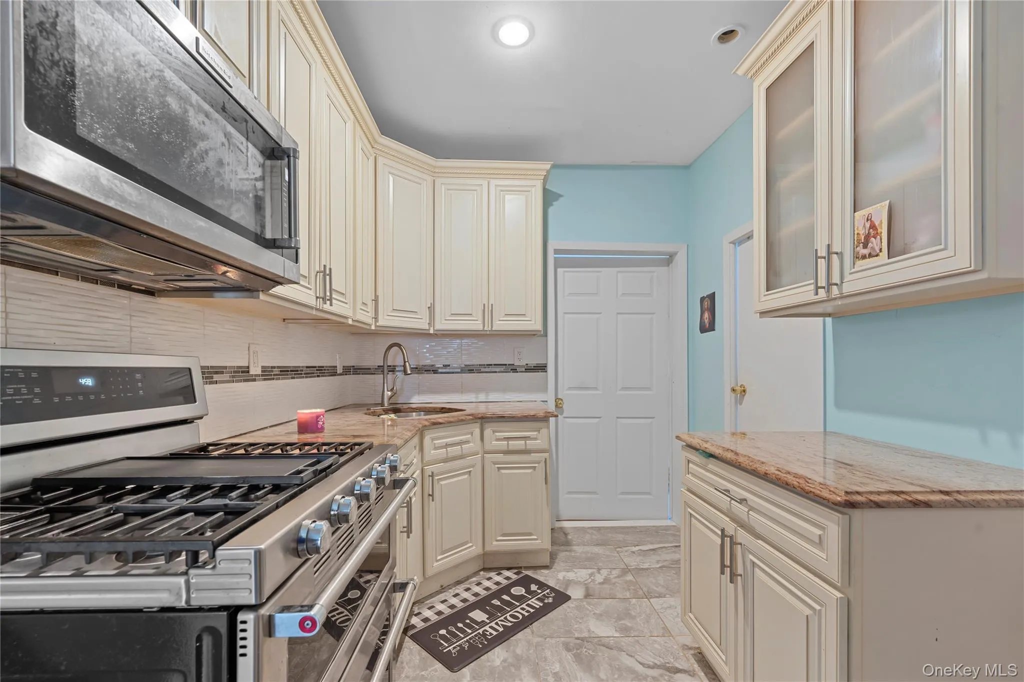 Kitchen with appliances with stainless steel finishes, light stone countertops, cream cabinetry, decorative backsplash, and glass insert cabinets Kitchen with appliances with stainless steel finishes, light stone countertops, cream cabinetry, decorative backsplash, and glass insert cabinets