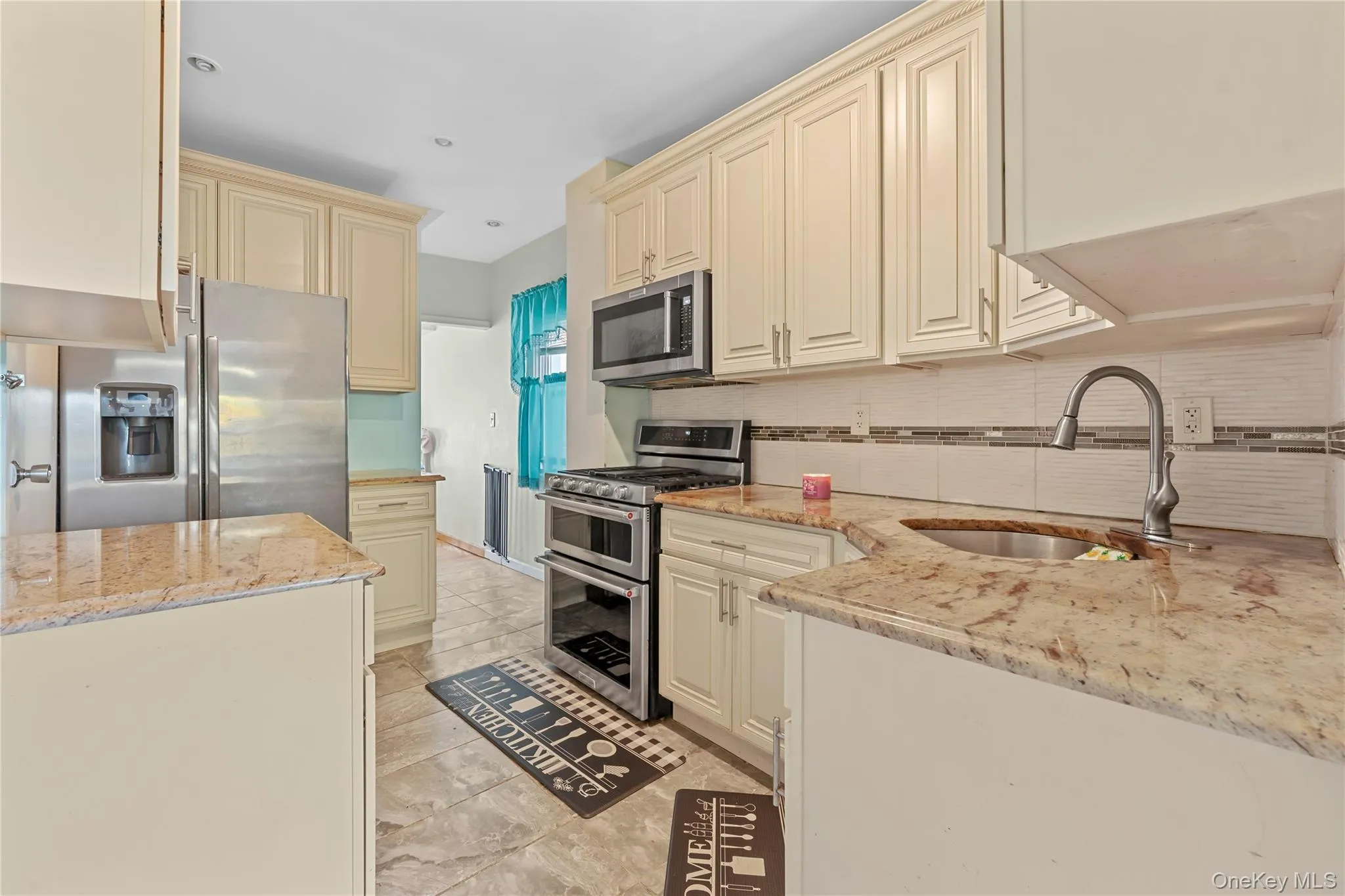 Kitchen featuring cream cabinets, light stone counters, stainless steel appliances, and decorative backsplash Kitchen featuring cream cabinets, light stone counters, stainless steel appliances, and decorative backsplash