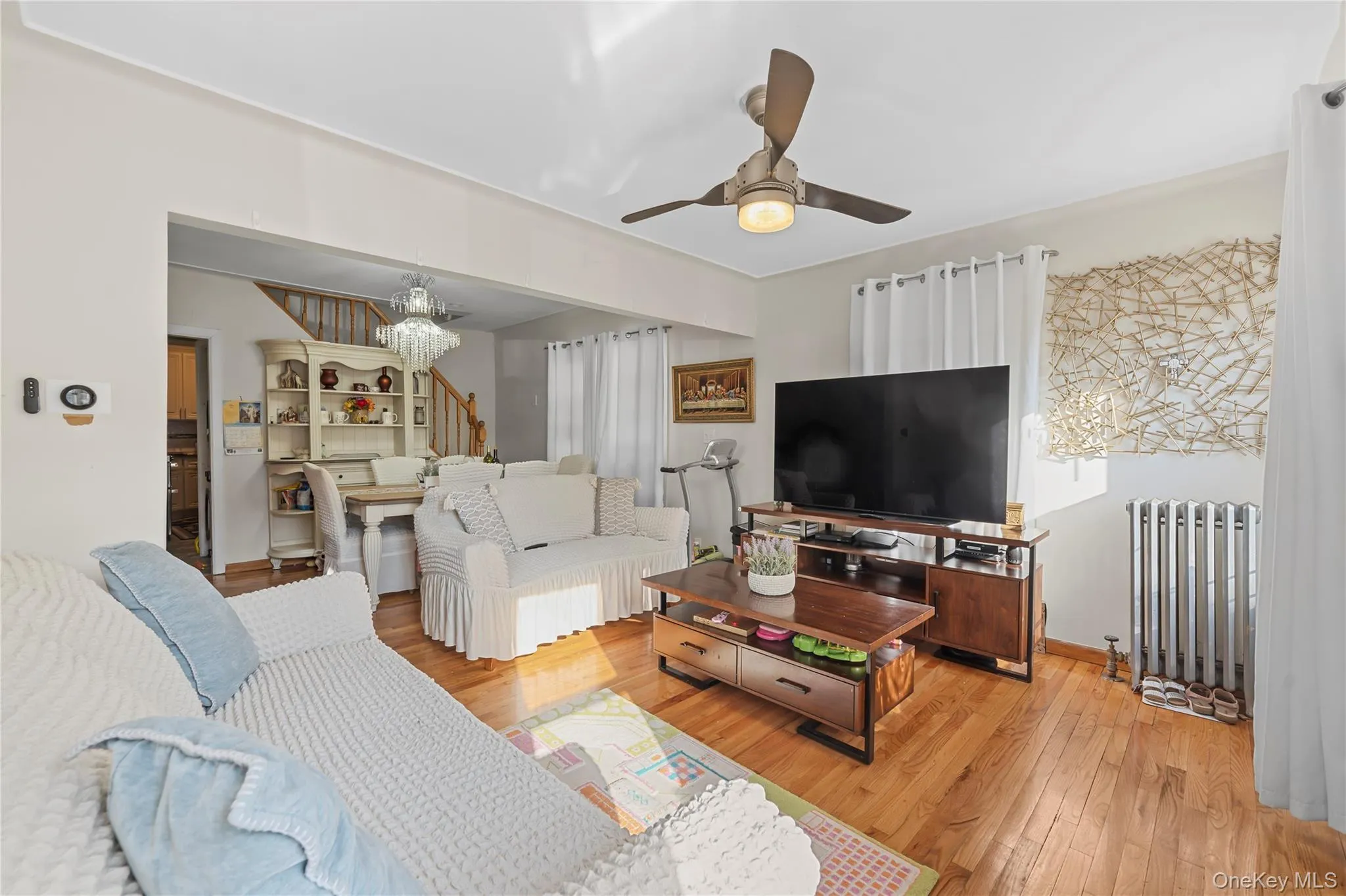 Living area featuring light wood-type flooring, radiator, ceiling fan, and a chandelier Living area featuring light wood-type flooring, radiator, ceiling fan, and a chandelier