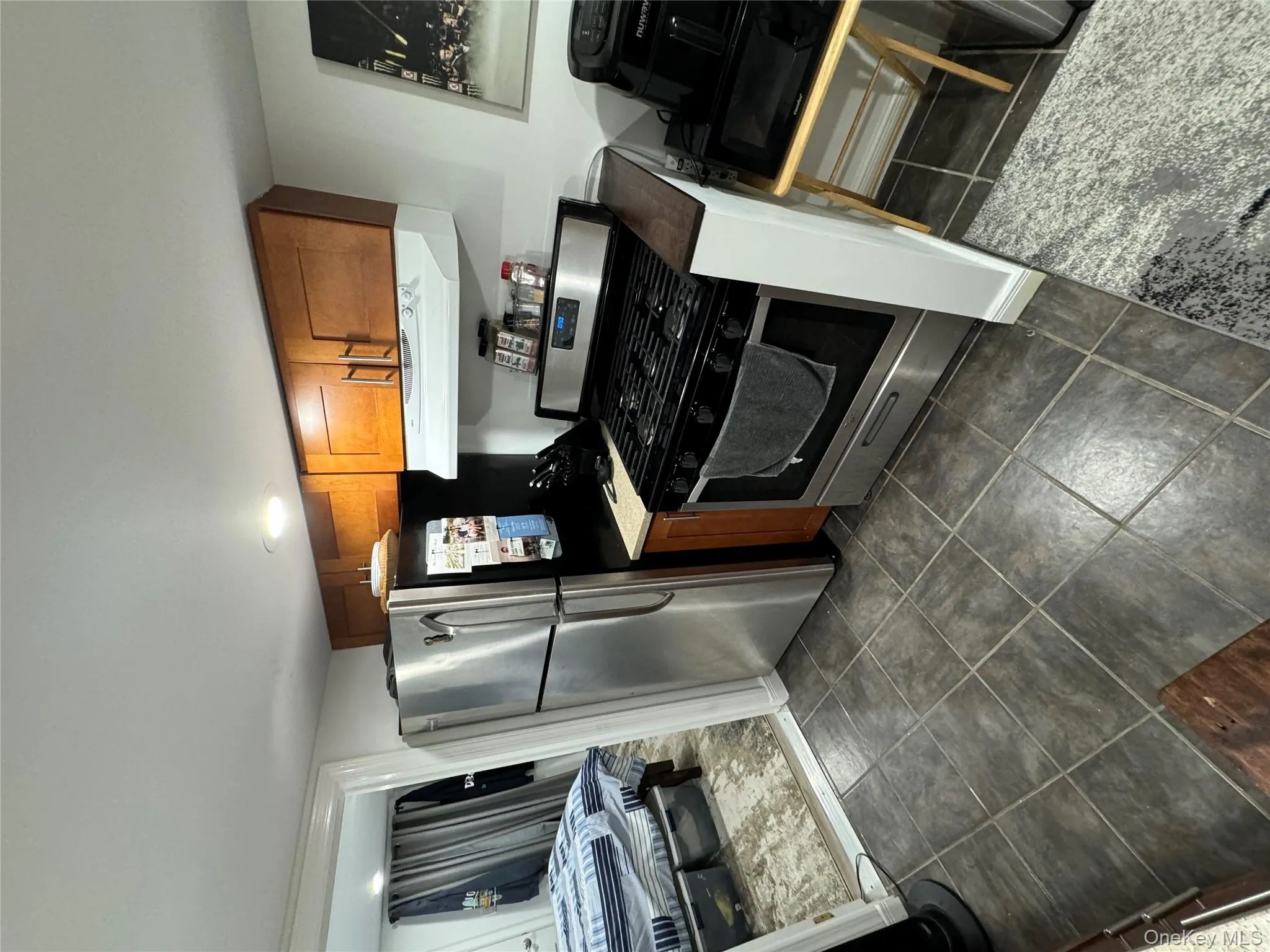 Kitchen featuring brown cabinets, stainless steel range oven, exhaust hood, dark tile patterned floors, and light countertops Kitchen featuring brown cabinets, stainless steel range oven, exhaust hood, dark tile patterned floors, and light countertops