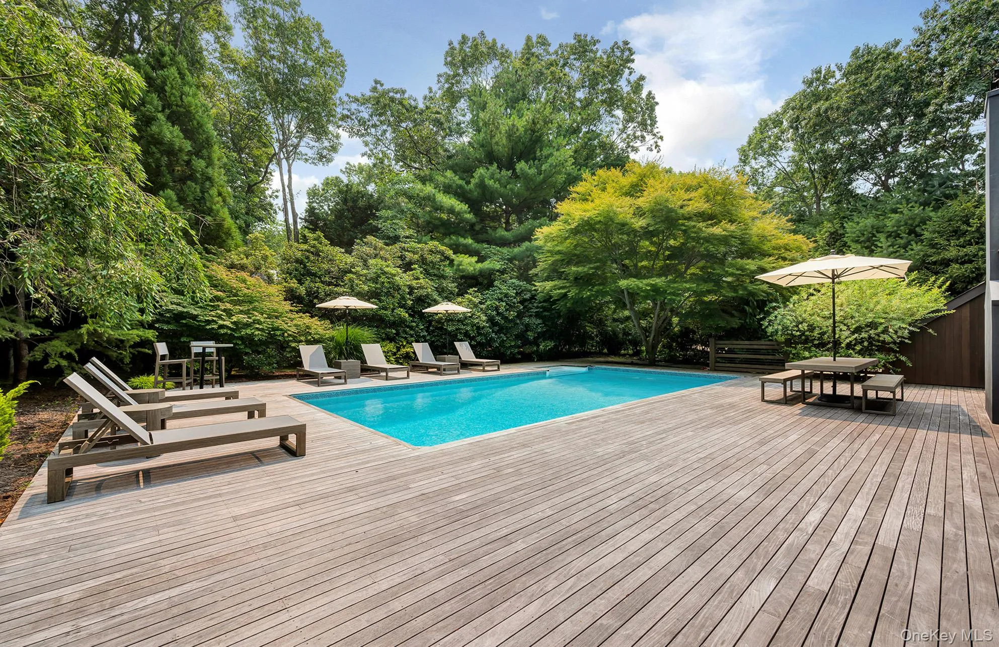 Outdoor pool with outdoor dining area, a wooden deck, and view of scattered trees Outdoor pool with outdoor dining area, a wooden deck, and view of scattered trees