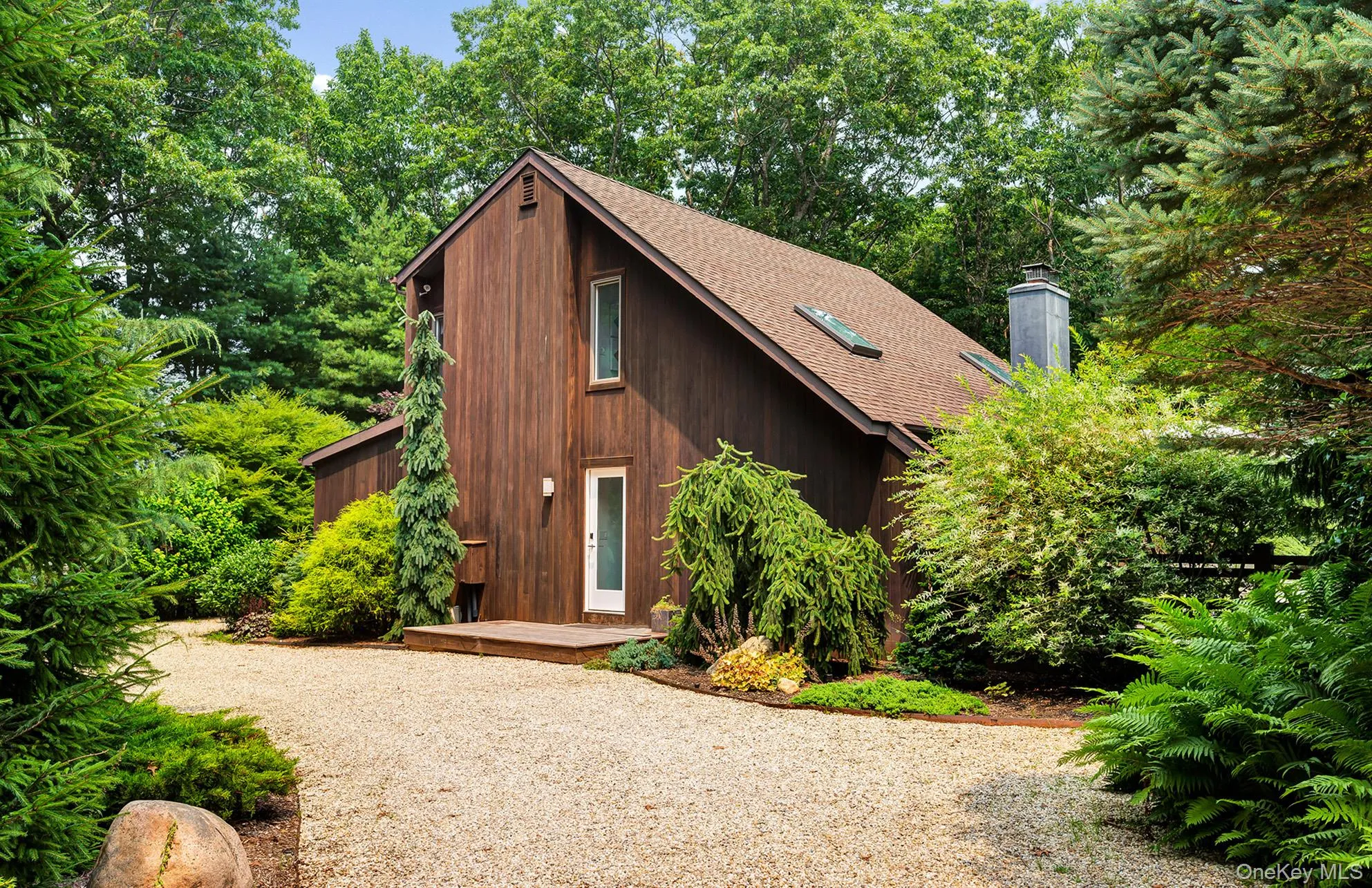 View of front of property with a wooden deck, a shingled roof, a chimney, and view of wooded area View of front of property with a wooden deck, a shingled roof, a chimney, and view of wooded area
