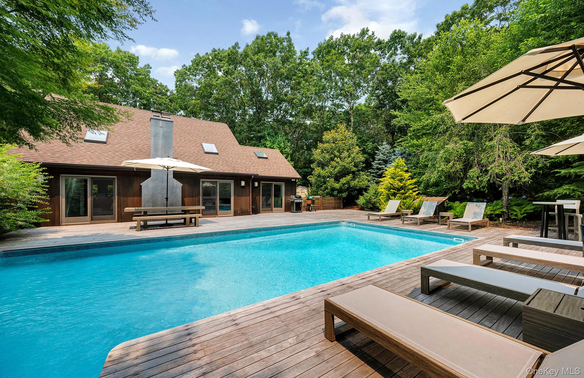Outdoor pool with a patio area, view of scattered trees, and grilling area Outdoor pool with a patio area, view of scattered trees, and grilling area