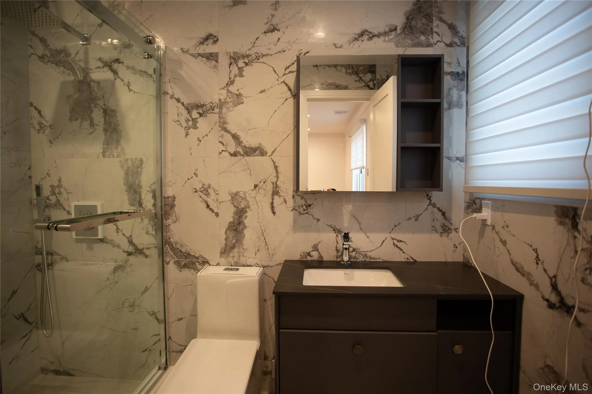 Bathroom featuring vanity, a marble finish shower, and tile walls Bathroom featuring vanity, a marble finish shower, and tile walls