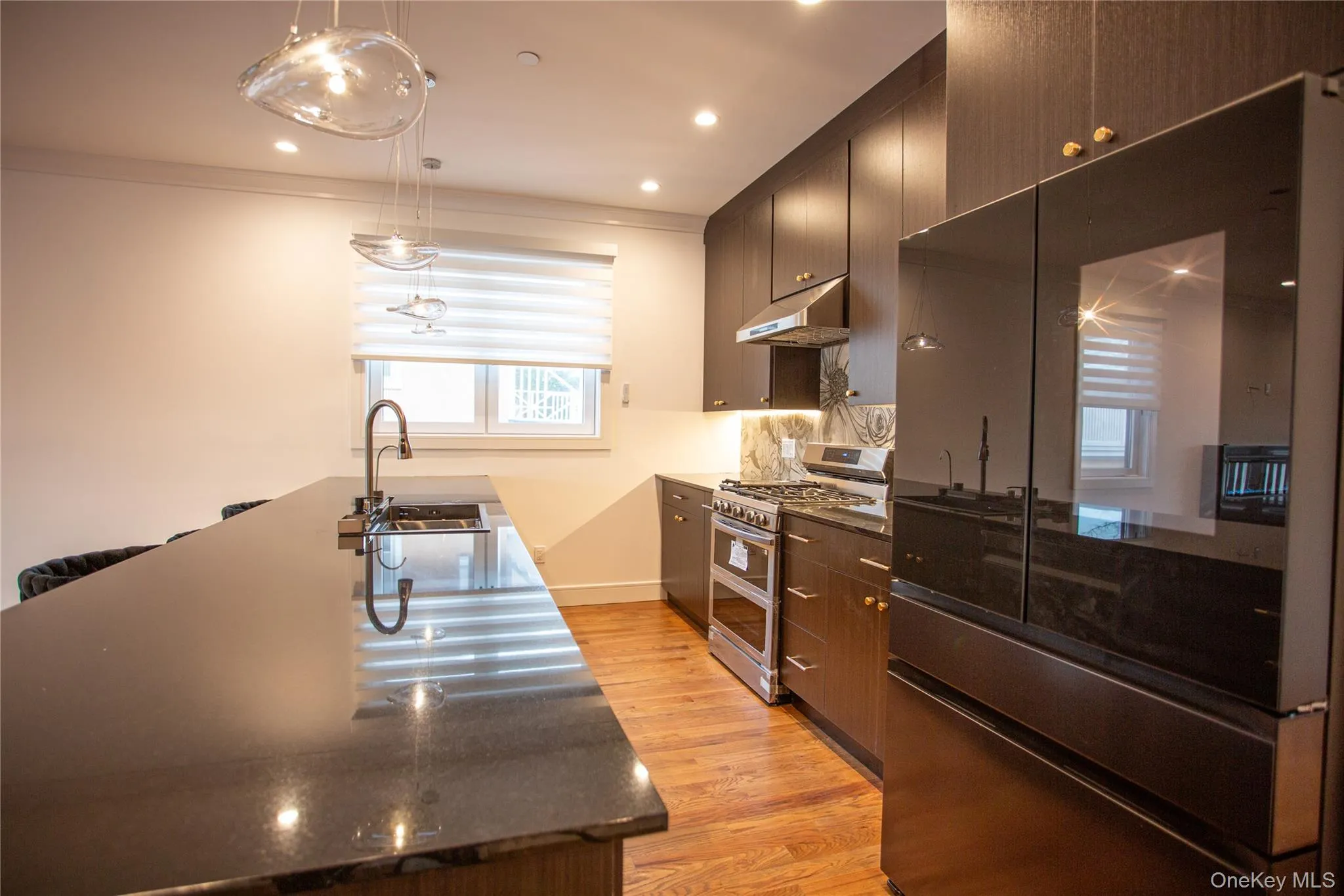 Kitchen with fridge, double oven range, decorative light fixtures, light wood-type flooring, and dark stone countertops Kitchen with fridge, double oven range, decorative light fixtures, light wood-type flooring, and dark stone countertops