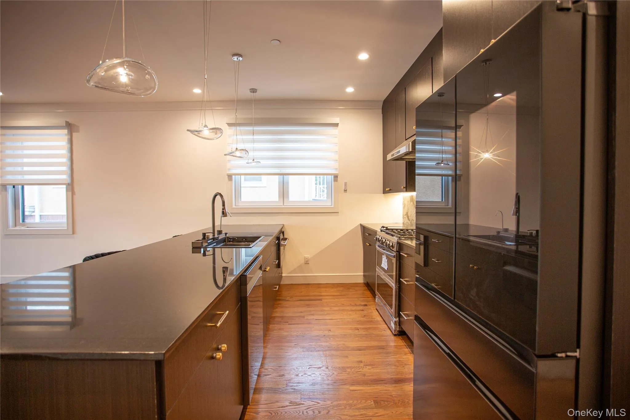 Kitchen with appliances with stainless steel finishes, decorative light fixtures, dark stone countertops, modern cabinets, and light wood-type flooring Kitchen with appliances with stainless steel finishes, decorative light fixtures, dark stone countertops, modern cabinets, and light wood-type flooring