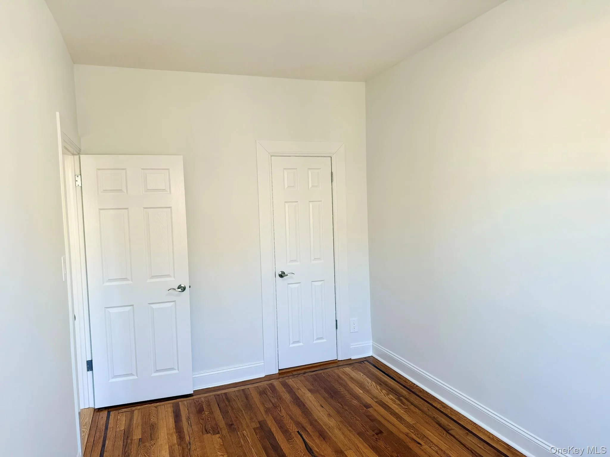 Unfurnished bedroom with dark wood finished floors and baseboards Unfurnished bedroom with dark wood finished floors and baseboards