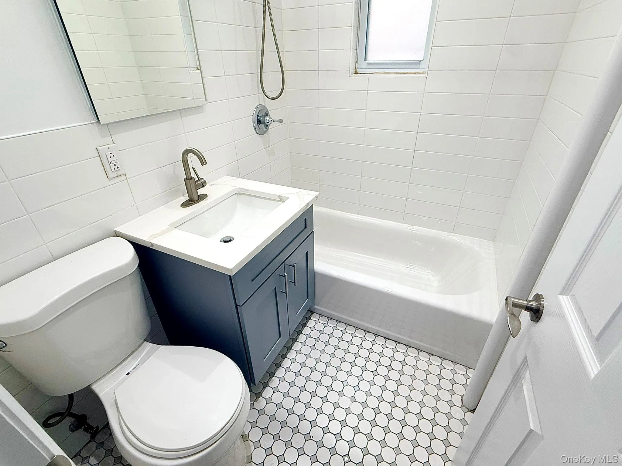 Bathroom with tile walls, vanity, shower / washtub combination, backsplash, and light tile patterned floors Bathroom with tile walls, vanity, shower / washtub combination, backsplash, and light tile patterned floors
