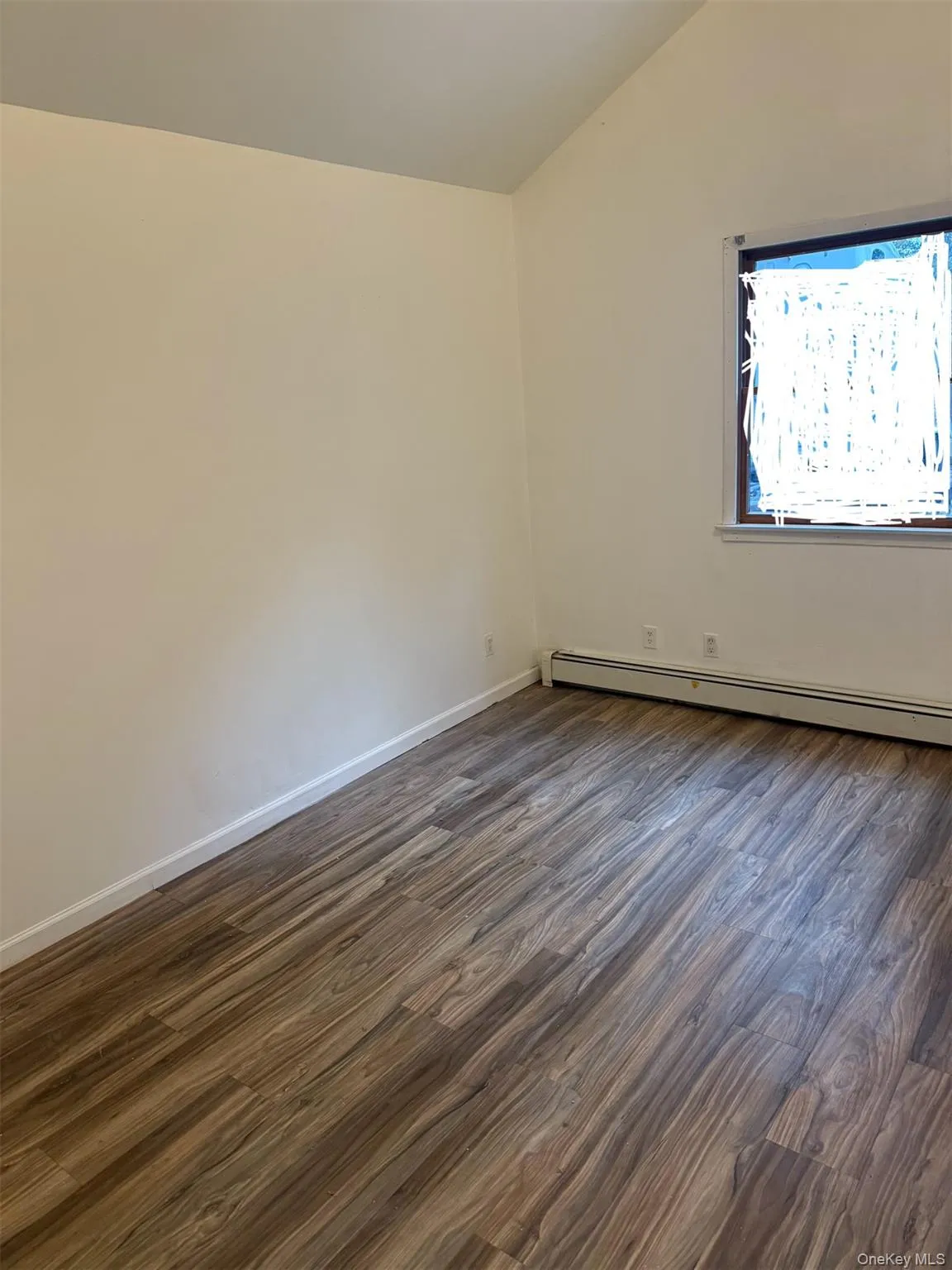 Empty room with dark wood-style flooring, baseboard heating, and lofted ceiling Empty room with dark wood-style flooring, baseboard heating, and lofted ceiling