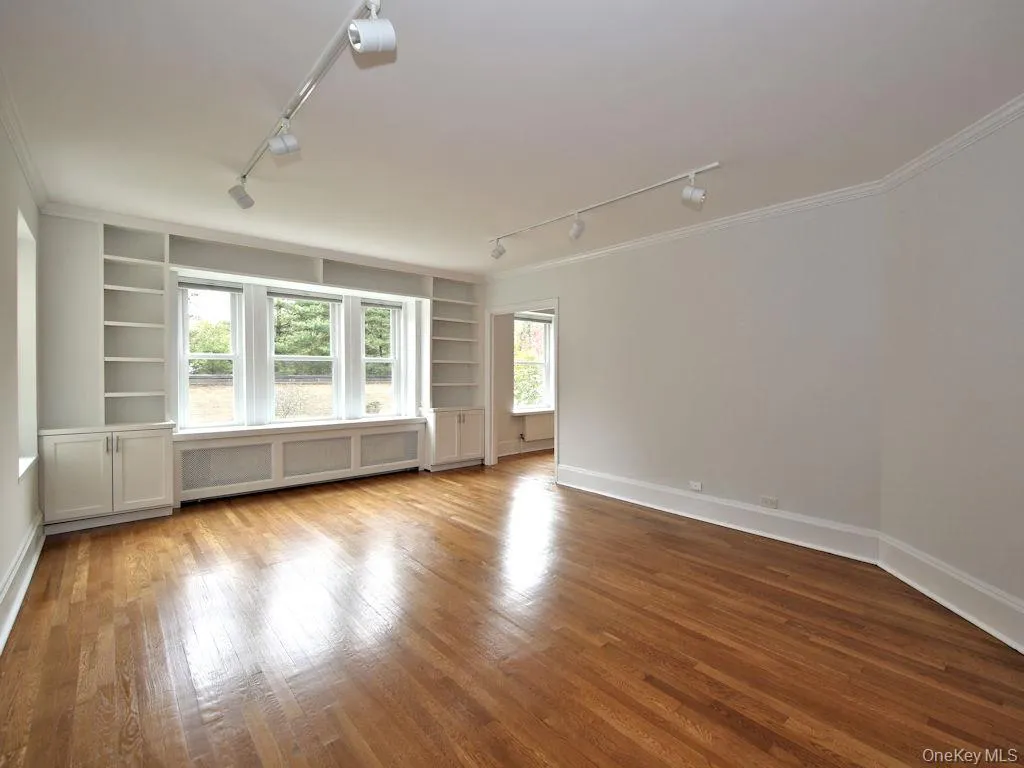 Empty room featuring built in features, rail lighting, radiator heating unit, and wood finished floors Empty room featuring built in features, rail lighting, radiator heating unit, and wood finished floors
