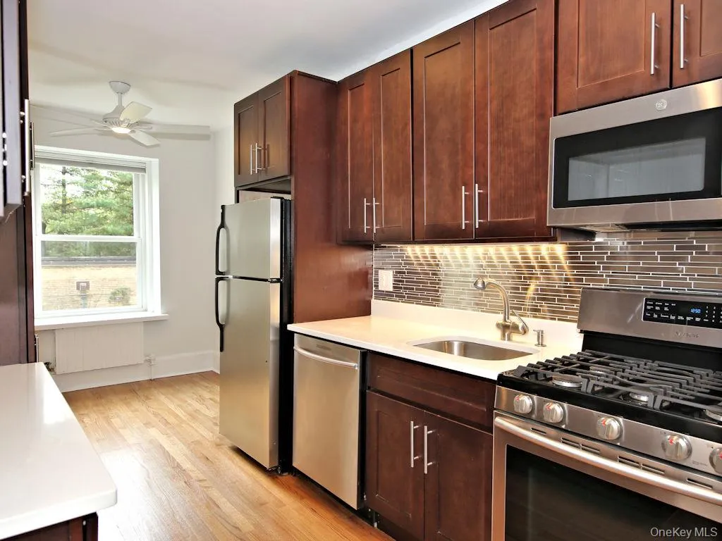 Kitchen with appliances with stainless steel finishes, light wood-style floors, radiator heating unit, light stone counters, and decorative backsplash Kitchen with appliances with stainless steel finishes, light wood-style floors, radiator heating unit, light stone counters, and decorative backsplash
